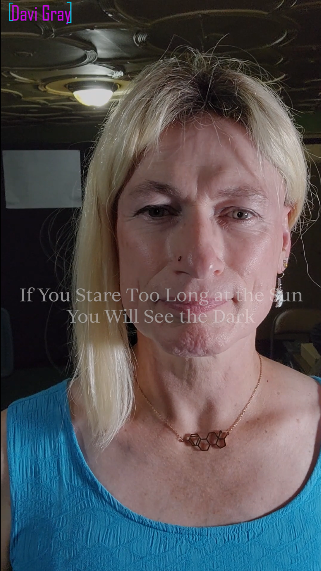 Photo of Davi Gray; she is wearing a bright blue dress, a necklace, and blond hair pulled back on one side.