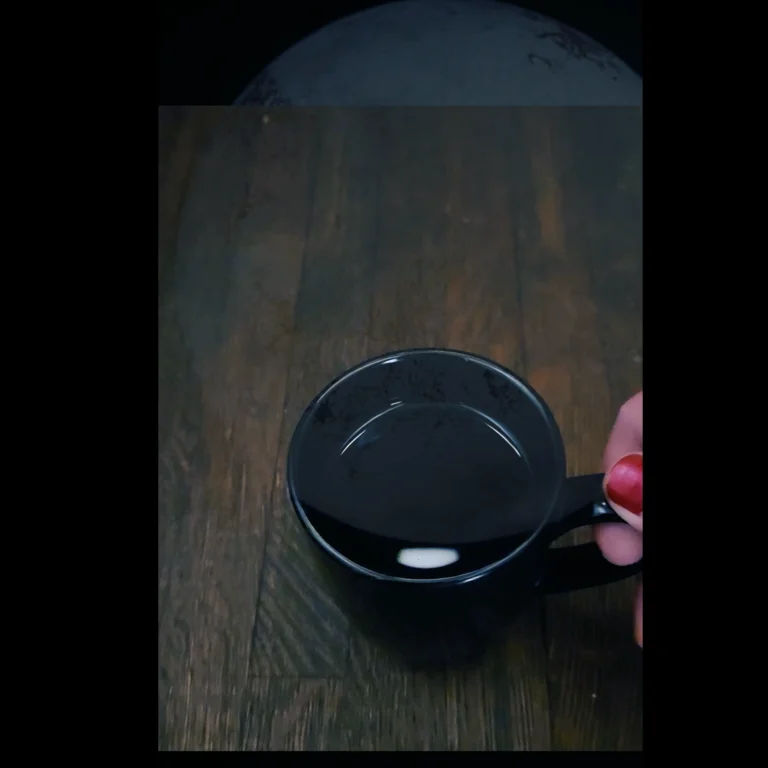 photograph of a hand, thumbnail painted red, holding the handle of a black mug filled with black liquid